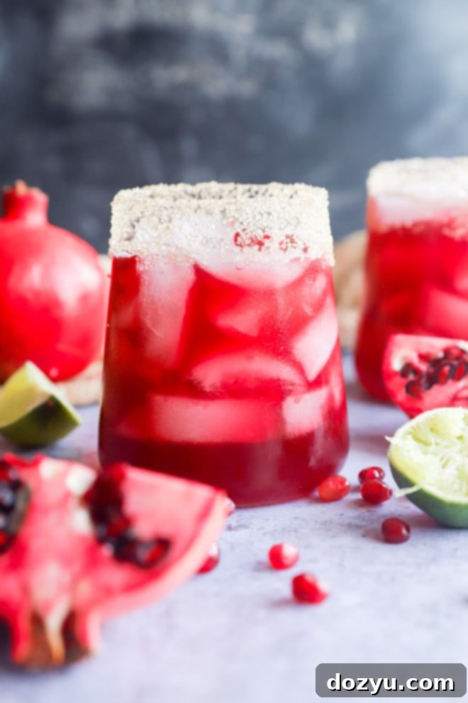 Two pomegranate margaritas in glasses, garnished with lime wedges and pomegranate arils.