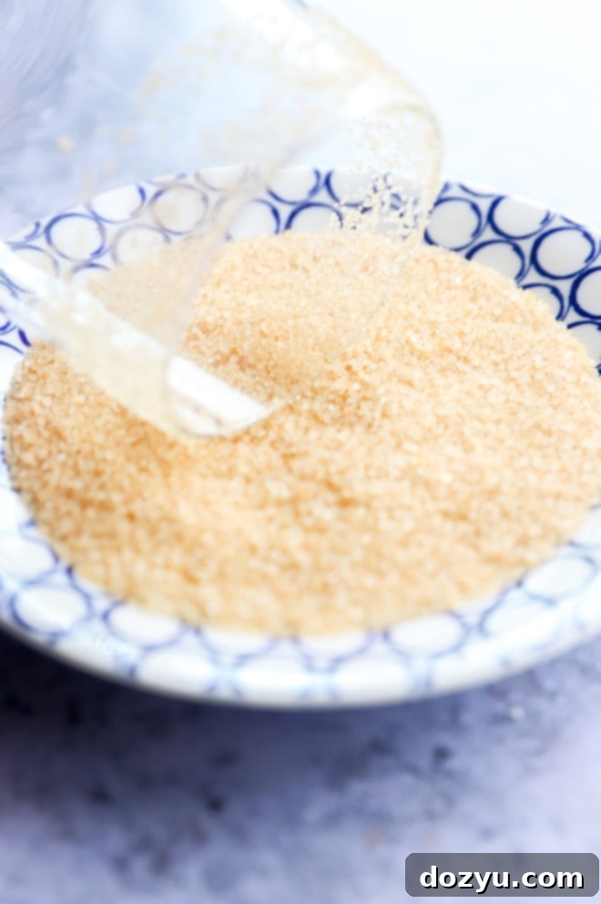 A hand carefully rimming the edge of a cocktail glass with turbinado sugar.