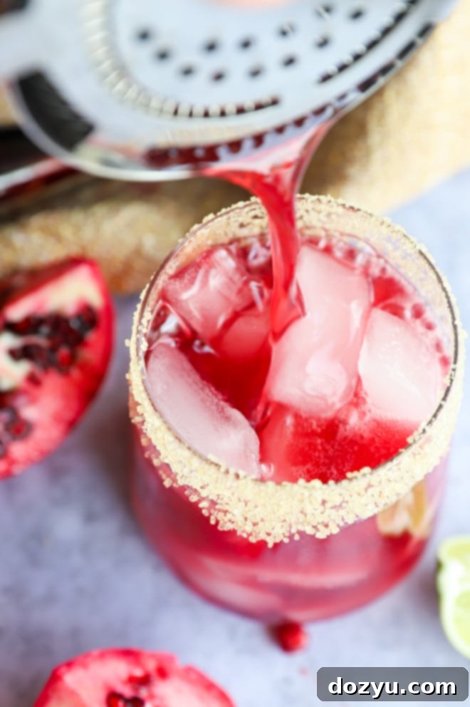 A pomegranate margarita being poured from a shaker into a prepared, ice-filled glass.