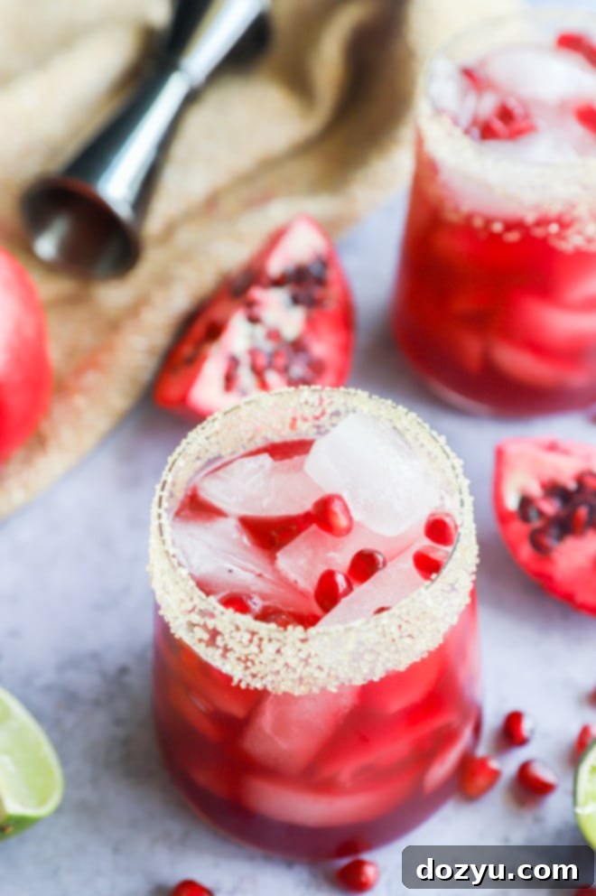 Two glasses of pomegranate margarita with lime and pomegranate aril garnishes.