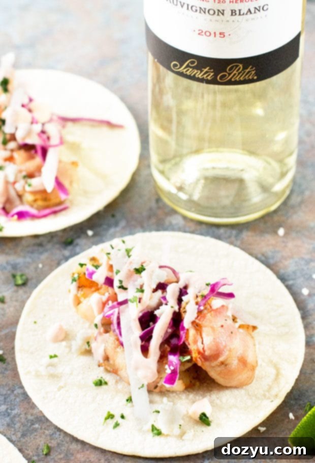 Side view of a hand holding a Grilled Bacon-Wrapped Shrimp Taco, showcasing its fresh fillings | cakenknife.com