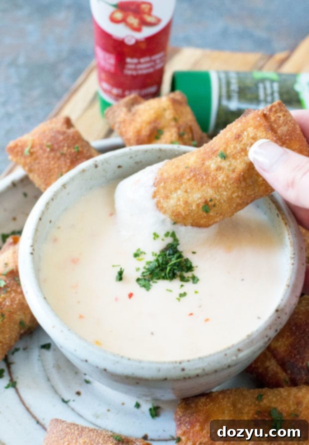 Chorizo Egg Rolls being dipped into creamy, spicy queso sauce.