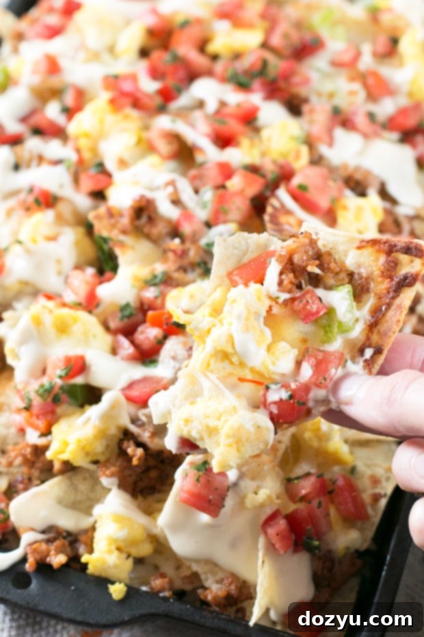Side view of Breakfast Italian Nachos, showcasing layers of savory toppings, melted cheese, and the rich Alfredo sauce drizzled over.