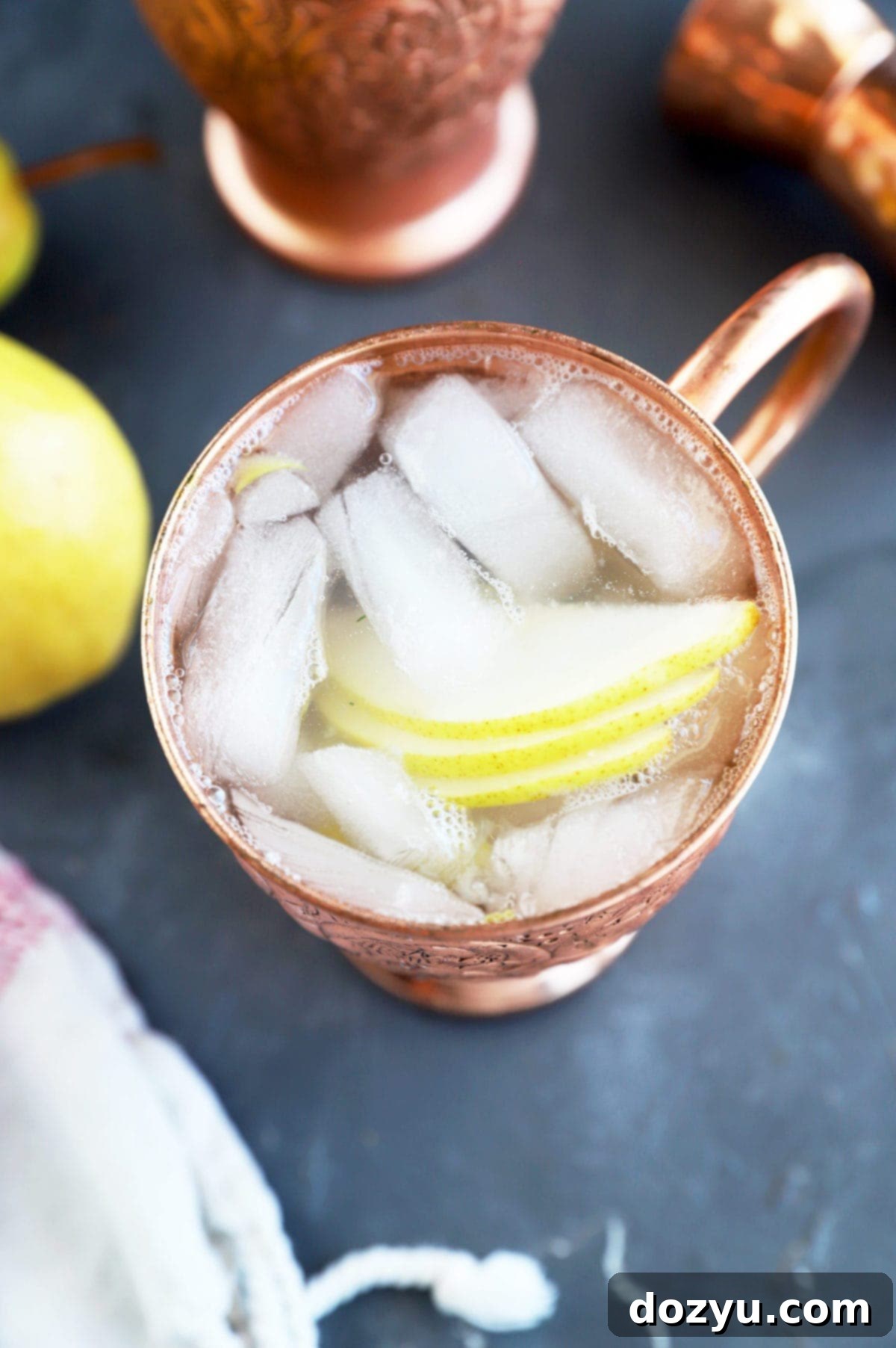 A copper mug filled with a Pear Moscow Mule, garnished with a pear fan, on a rustic background.