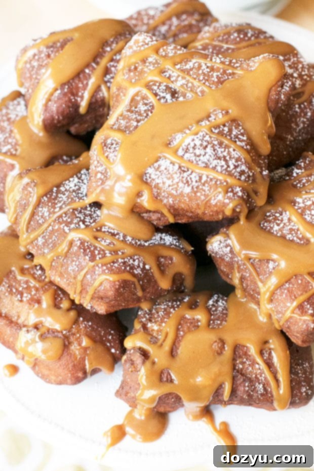 A close-up of a plate piled high with golden Pumpkin Spice Beignets and a stream of salted caramel