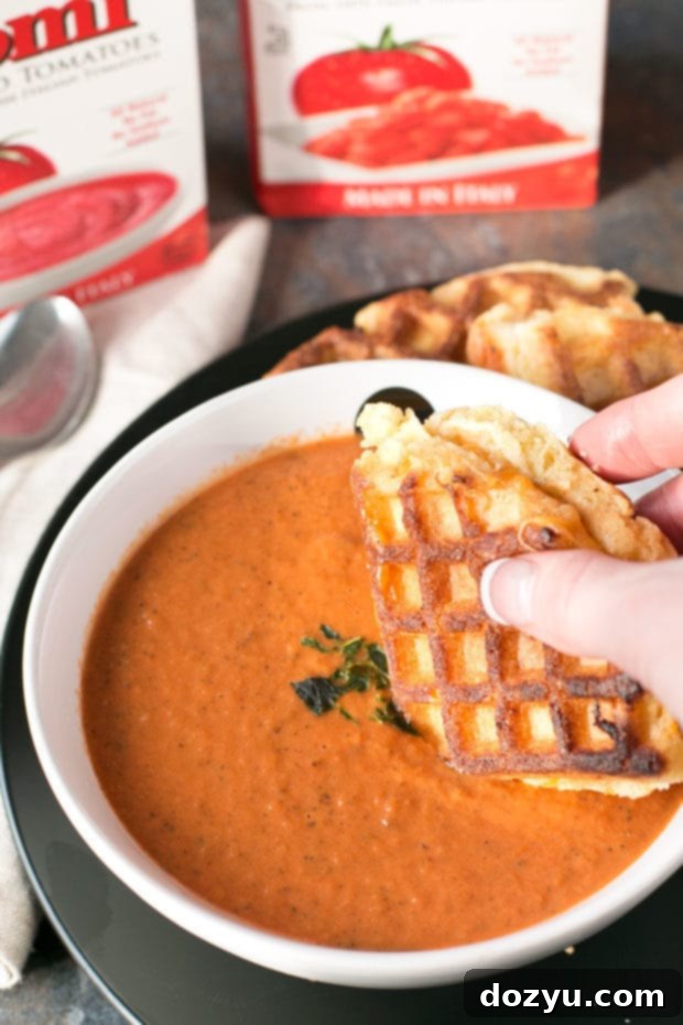 Warm, inviting Cornbread Waffle Grilled Cheese Sandwich being dipped into rich Tomato Basil Soup.
