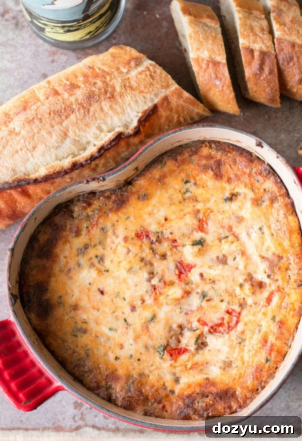 A close-up shot of bubbling Spicy Lasagna Dip, highlighting the gooey cheese, roasted tomatoes, and bits of spicy Italian sausage. So good, you won't miss the lasagna noodles!