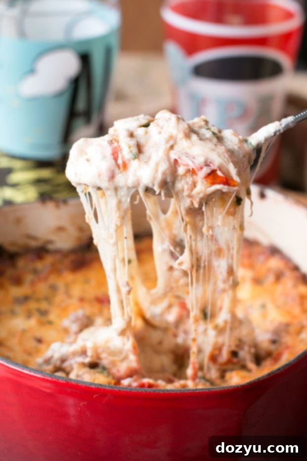 Spicy Lasagna Dip served hot in a baking dish, showcasing its melted cheese, herbs, and chunks of spicy Italian sausage, ready for dipping.