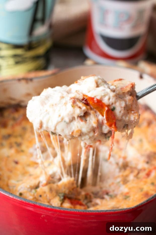 A serving of Spicy Lasagna Dip, incredibly cheesy and vibrant, featuring roasted tomatoes and a generous amount of spicy Italian sausage. The perfect appetizer for any occasion.
