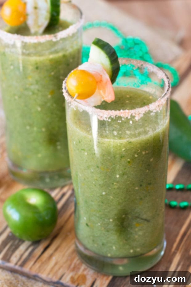 Three Spicy Green Bloody Mary cocktails arranged on a wooden table, showcasing garnishes like celery, cucumber, and lime slices.