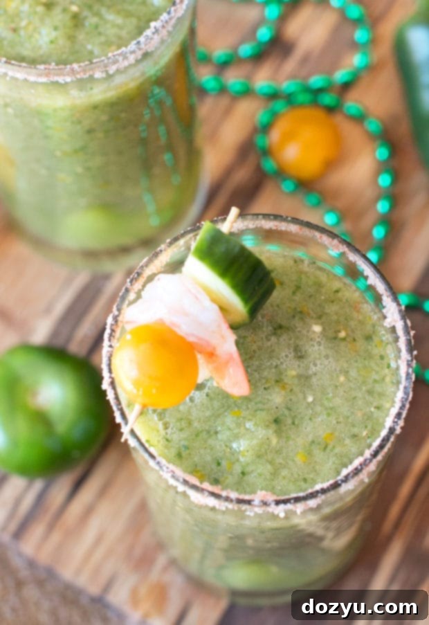 A single Spicy Green Bloody Mary cocktail, garnished with a slice of cucumber and a cherry tomato, ready for serving on a light background.