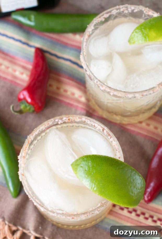 Two glistening Chili Lime Margaritas in elegant glasses, garnished with fresh lime, with a blurred festive background.