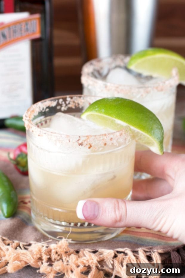 Two Chili Lime Margaritas with chili-rimmed glasses and lime garnishes, ready to be enjoyed on a light-colored surface.