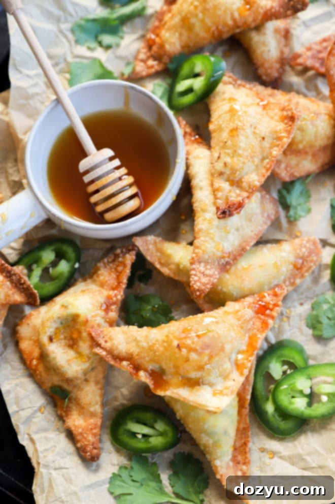Avocado Jalapeño Popper Wonton Bites 2 Overhead image of crispy golden-brown jalapeño popper avocado wontons on a baking sheet, drizzled with hot honey and garnished with fresh jalapeños