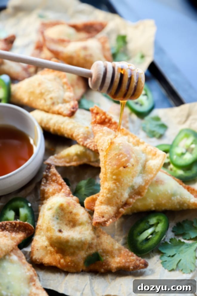 Avocado Jalapeño Popper Wonton Bites 3 Close-up image of a hand drizzling hot honey over a platter of freshly fried jalapeño popper avocado wontons