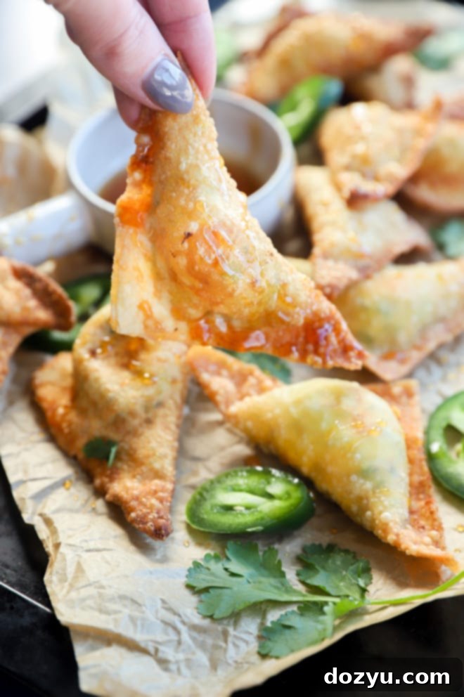 Avocado Jalapeño Popper Wonton Bites 10 Close-up of a hand holding a single perfectly fried jalapeño cream cheese wonton, showing its crispy texture