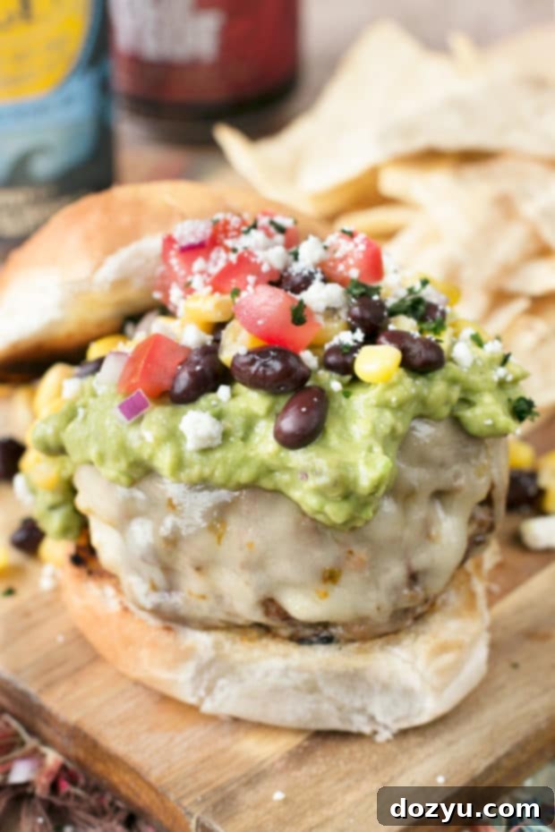 A hand presenting a Southwestern Guacamole Burger, showing off its rich layers of guacamole, cheese, corn, and perfectly grilled patty.