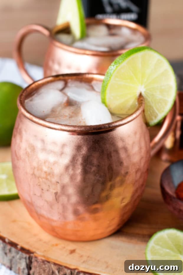 A beautifully crafted Spicy Mezcal Mule cocktail in a chilled copper mug, garnished with a vibrant lime wheel, on a rustic surface. Perfect for any autumn gathering or an adventurous cocktail hour.