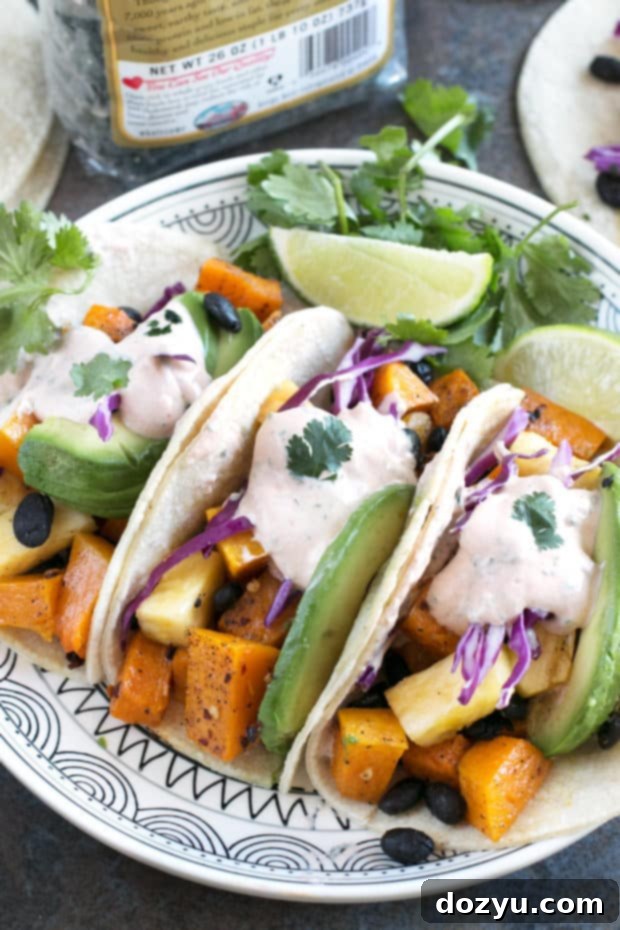 Roasted Butternut Squash Black Bean Tacos ready to be served on a vibrant patterned plate. Features orange squash, black beans, purple cabbage, green avocado, and a creamy sauce. #vegetarian #healthy #tacotuesday #sponsored