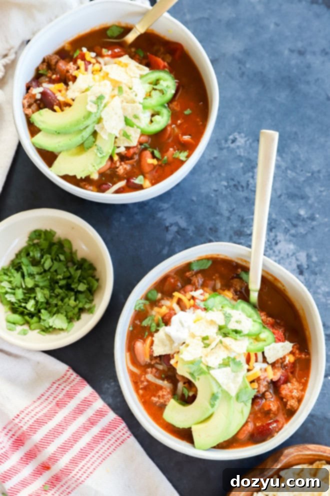 Bowls of soup with spoons and toppings on the side, showcasing the delicious Spicy Taco Chili.