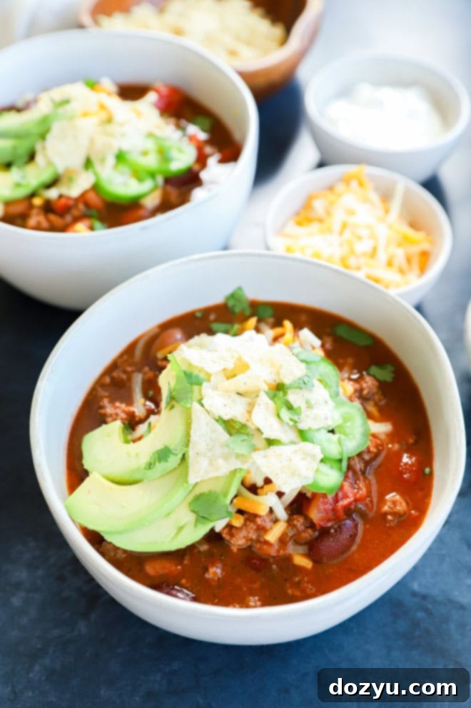 Bowls of spicy taco chili ready to be served, accompanied by various toppings and a bowl of cheese.