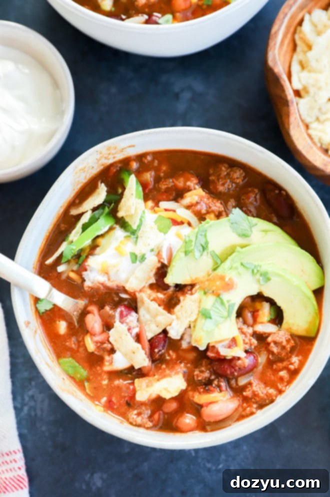 A close-up shot of a bowl of spicy taco chili, garnished with fresh toppings and a spoon resting inside.
