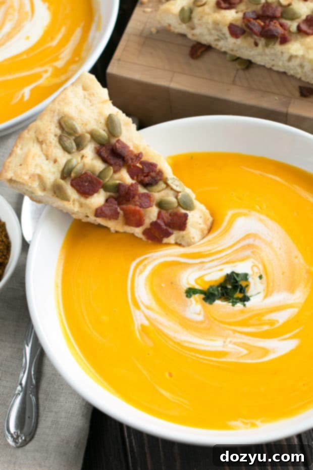 Creamy Curried Roasted Butternut Squash Soup served with a slice of Bacon Pumpkin Seed Bread on a rustic table, perfect for fall and Thanksgiving