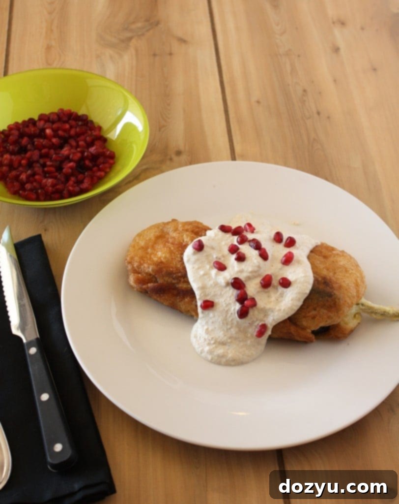 A beautifully presented Chiles en Nogada, showcasing the green pepper, white sauce, and red pomegranate seeds.
