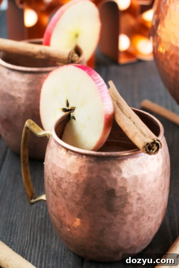 Close-up of Gingerbread Bourbon Punch in copper mugs with apple and cinnamon garnish. Perfect large batch holiday cocktail.