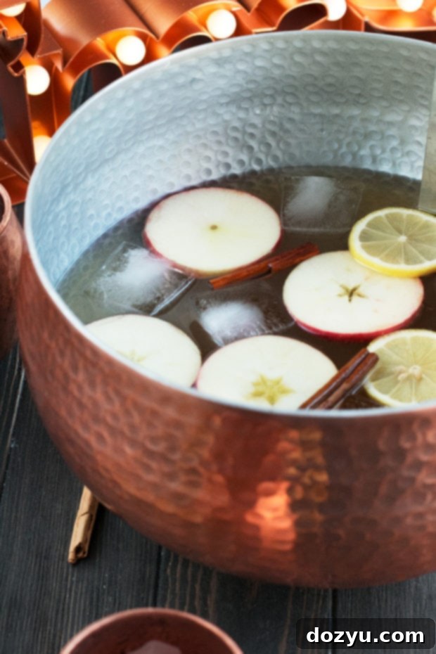 Six copper mugs filled with Gingerbread Bourbon Punch, garnished with apple slices and cinnamon sticks, on a festive holiday table.