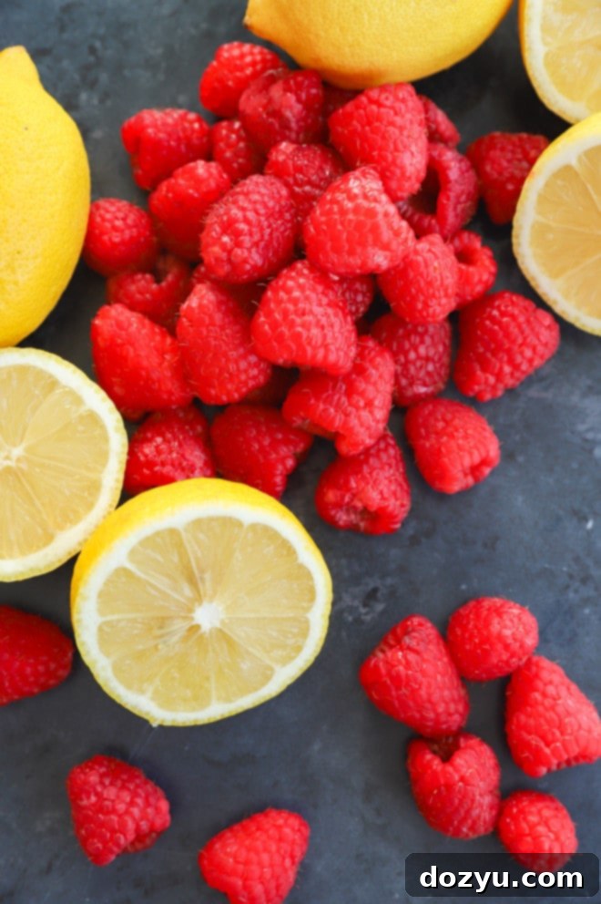 Selection of fresh ingredients for a raspberry vodka lemonade, including ripe raspberries, whole lemons, granulated sugar, and a bottle of vodka.