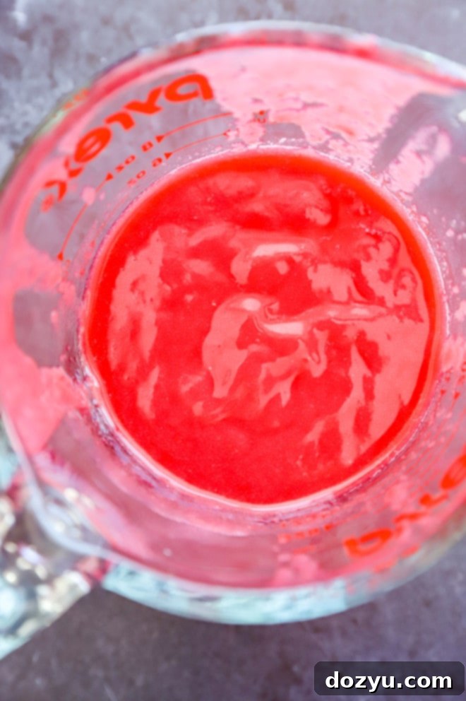 Close-up of freshly made raspberry puree in a glass pitcher, showcasing its vibrant red color and smooth texture.