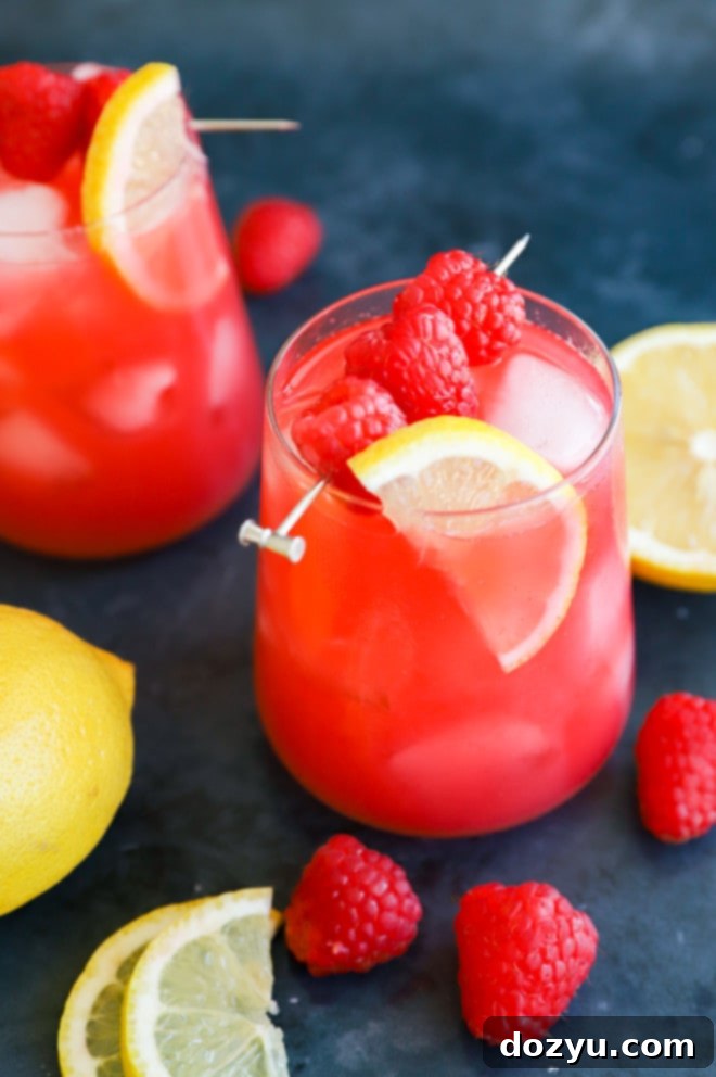 Close-up of a rustic wooden surface with a glass of Raspberry Vodka Lemonade and scattered fresh raspberries.
