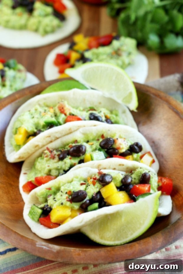 Freshly prepared Guacamole Tacos on a wooden board with lime wedges