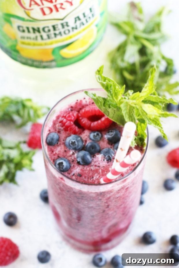 A glass of the frozen mocktail alongside fresh berries and mint leaves.