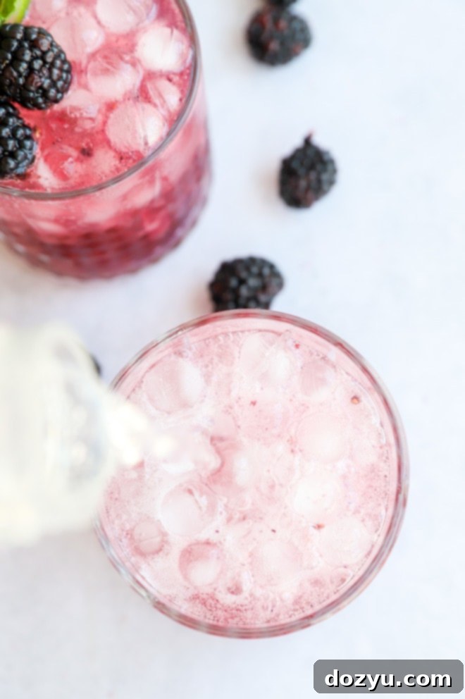 Image demonstrating pouring soda water into a cocktail glass filled with the blackberry gin mixture and ice, completing the fizzy drink.