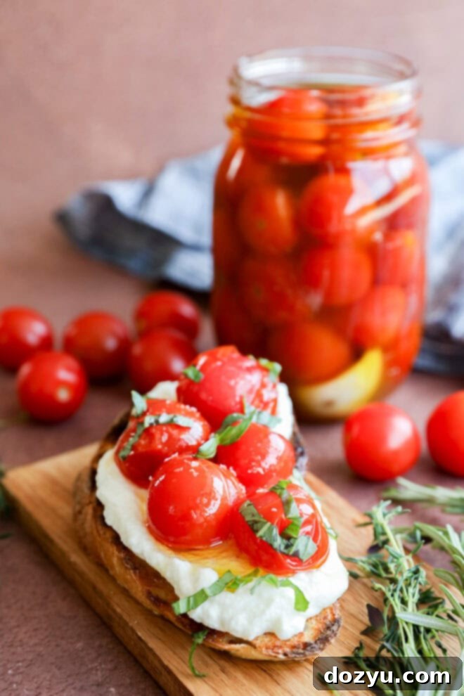 A slice of toasted bread topped with fresh mozzarella, cherry tomatoes, and basil sits on a wooden board. In the background, a jar of cherry tomato confit and scattered fresh tomatoes and herbs add vibrant color to the scene.