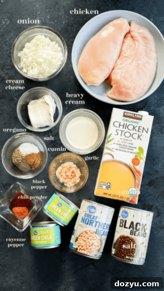 Dreamy Slow Cooker White Chicken Chili 3 Various ingredients for slow cooker white chicken chili laid out in small bowls, including chicken, beans, spices, onion, garlic, and cream.
