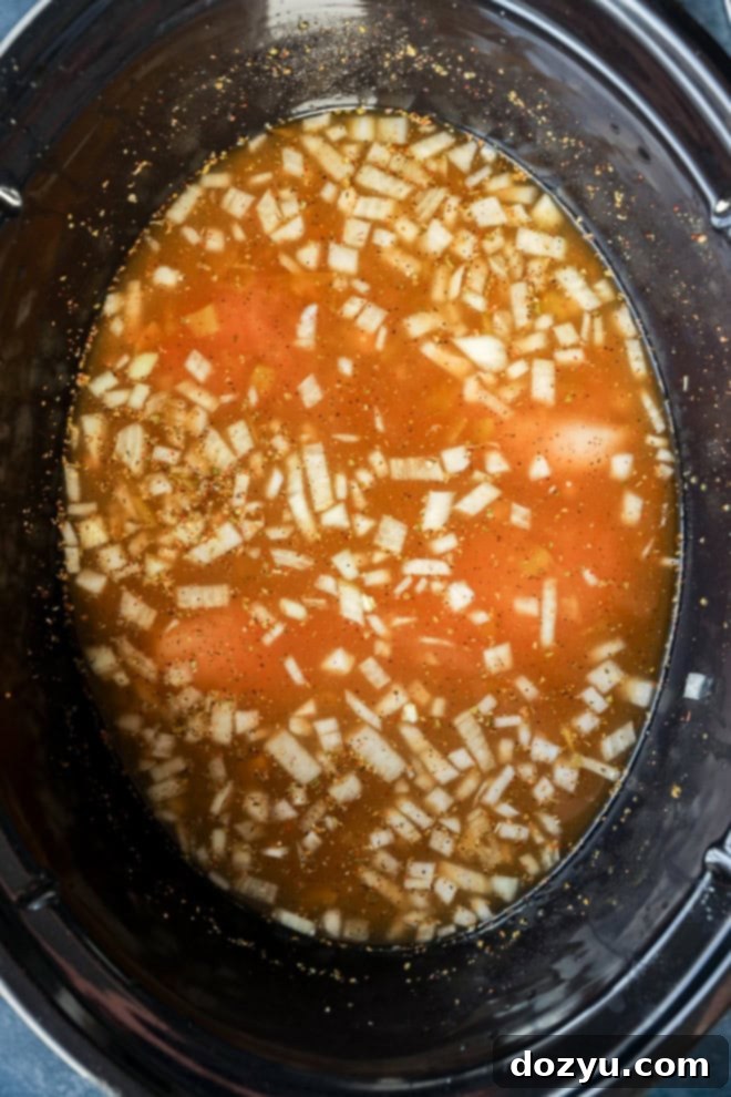 Dreamy Slow Cooker White Chicken Chili 5 All ingredients for white chicken chili, including chicken, beans, spices, and liquids, combined in a slow cooker insert before cooking.
