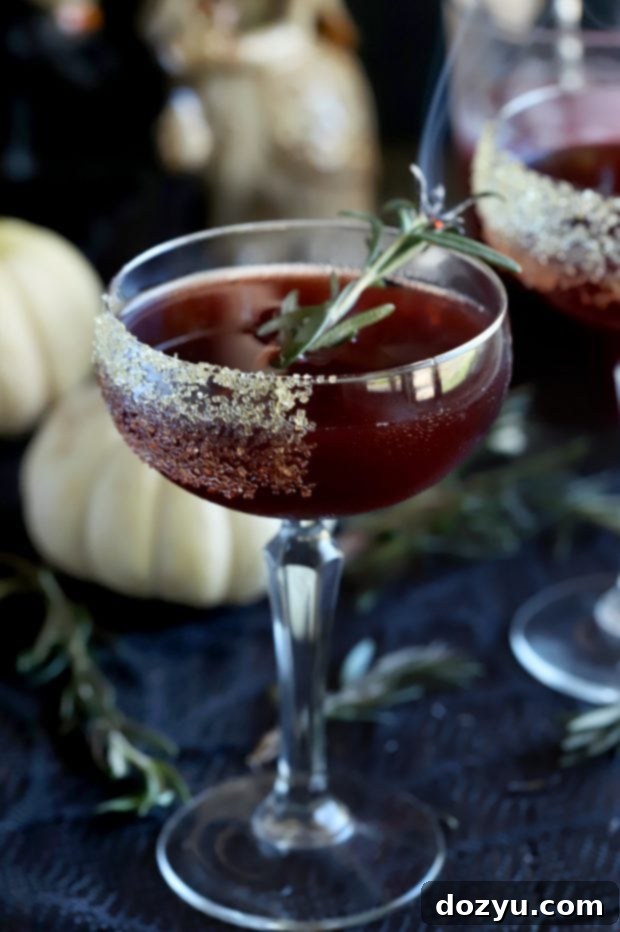 Spooky Pomegranate Cocktail on a table adorned with pumpkins and fresh rosemary, ready for serving