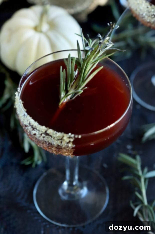 Spooky Pomegranate Drink in a coupe glass, close-up to show the charred rosemary garnish
