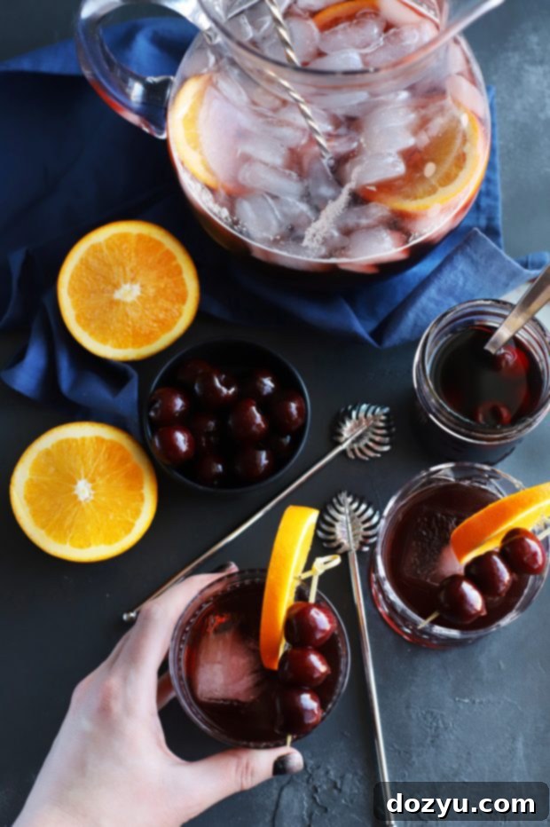A cocktail glass filled with Perfect Manhattan Punch, elegantly garnished with an orange slice and brandied cherries, on a rustic wooden surface