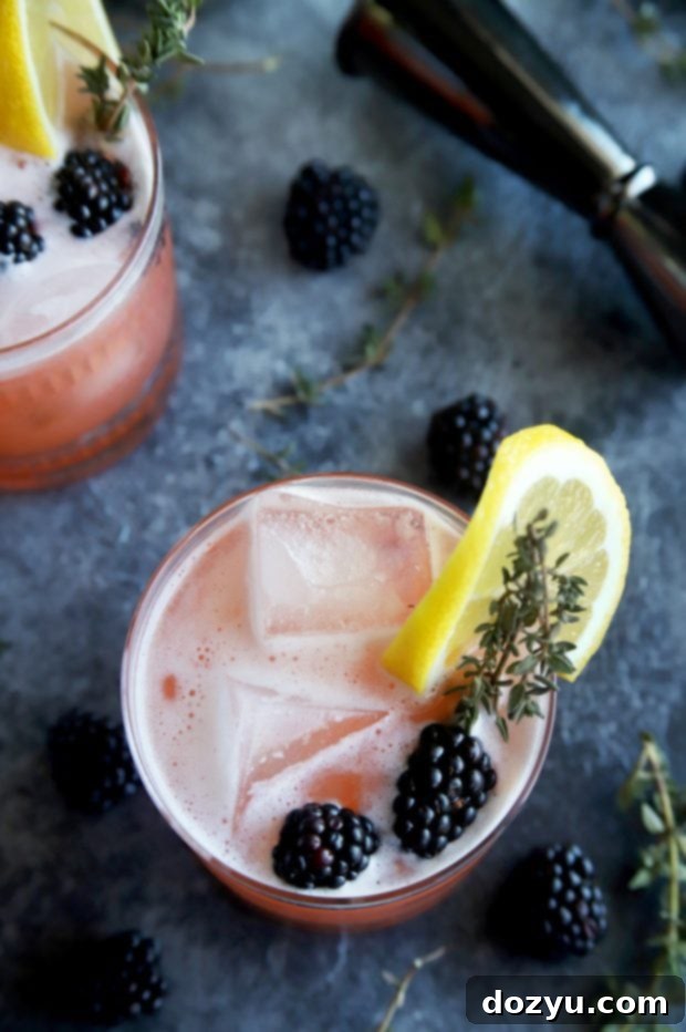 The Bramble & Thyme Irish Whiskey Sour 5 A close-up of a hand holding a Blackberry Thyme Irish Whiskey Sour cocktail garnished with blackberries and a sprig of thyme.