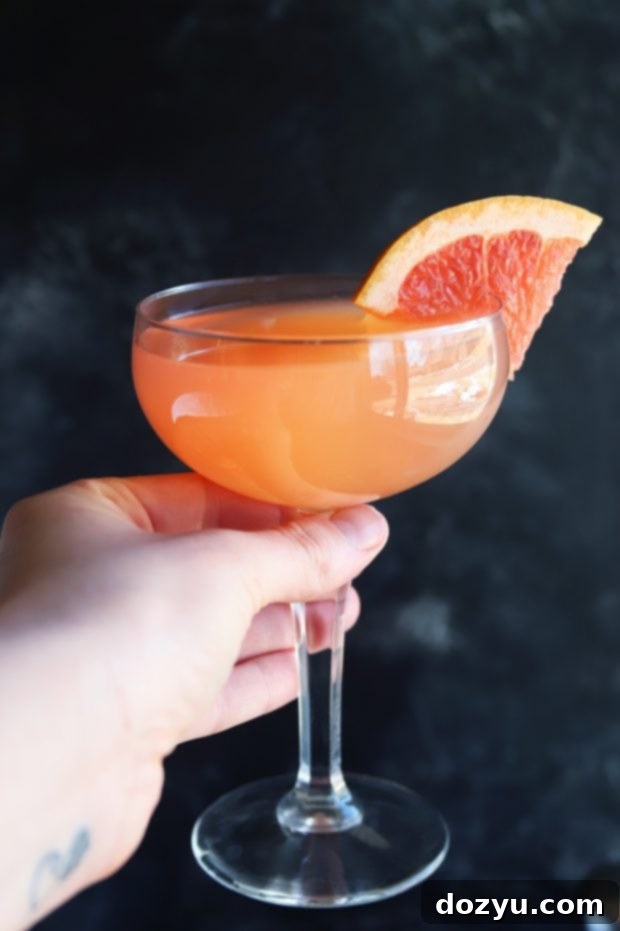 Rosé Grapefruit Sparkler 4 Close-up of a hand holding a Sparkling Grapefruit Rosé Cocktail, showcasing the beautiful pink hue and grapefruit garnish.