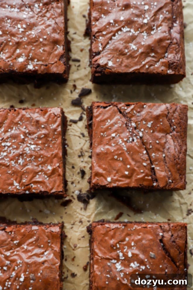 Perfectly cut triple chocolate brownies arranged in neat rows on parchment paper, showcasing their fudgy texture and shiny tops.