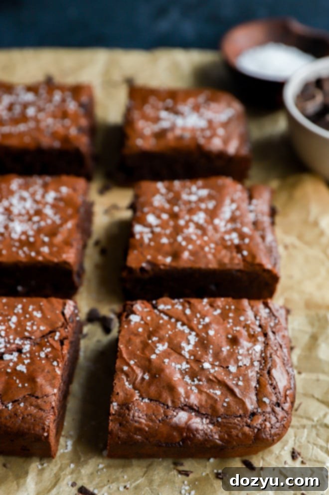 Close-up of a cut triple chocolate brownie on parchment paper, highlighting its fudgy interior and glossy crust, with a sprinkle of salt visible on top.