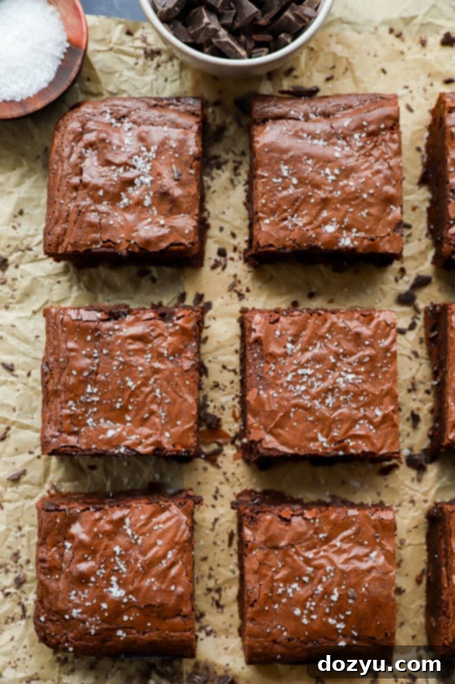 Several neatly cut triple chocolate brownies are scattered on parchment paper, with visible chocolate chips and a slightly crinkled top crust.