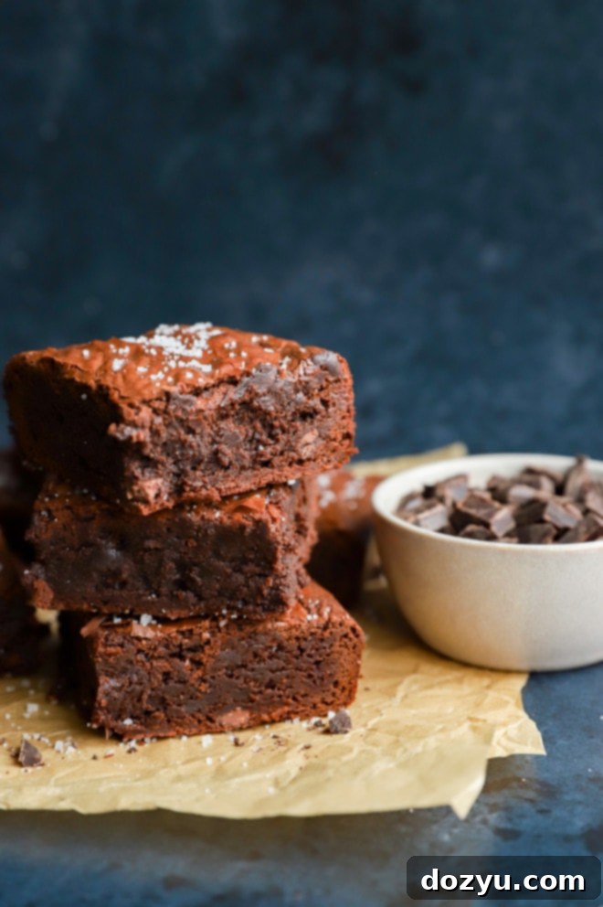 A stack of dark, rich brownies dusted with cocoa powder and powdered sugar, suggesting a decadent chocolate dessert.