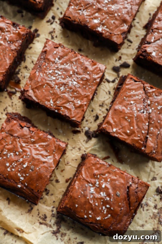 A close-up shot of a single, perfectly cut triple chocolate brownie with a glossy, crinkled top, showcasing its rich, fudgy texture.