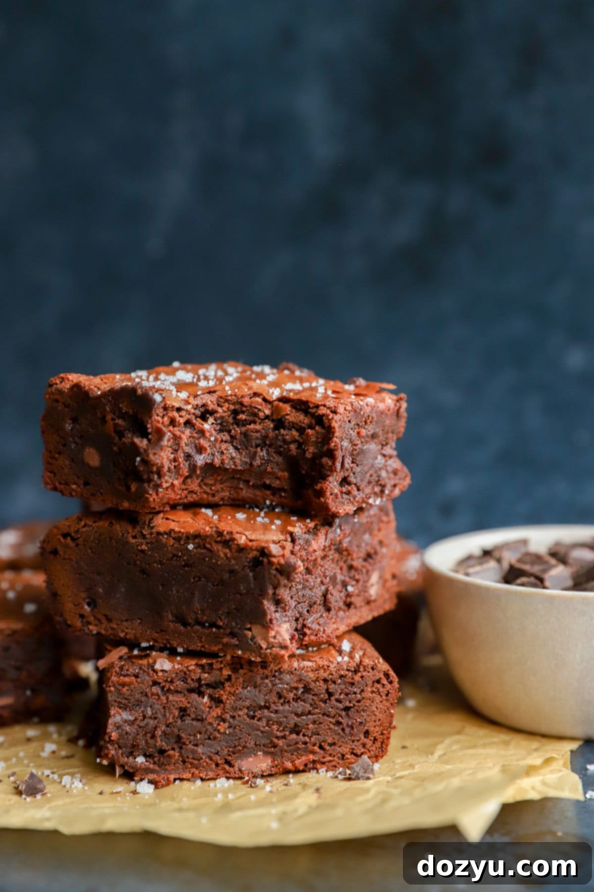 A beautiful stack of three fudgy triple chocolate brownies, perfectly cut and ready to be enjoyed, resting on parchment paper.